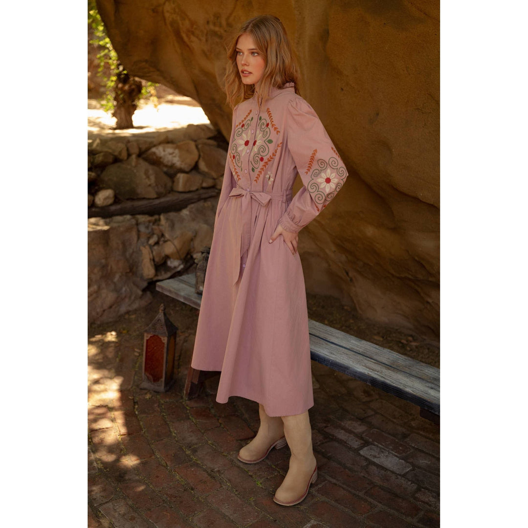 A soft pink embroidered shirtdress trench coat with red and green patterns on the chest and sleeves