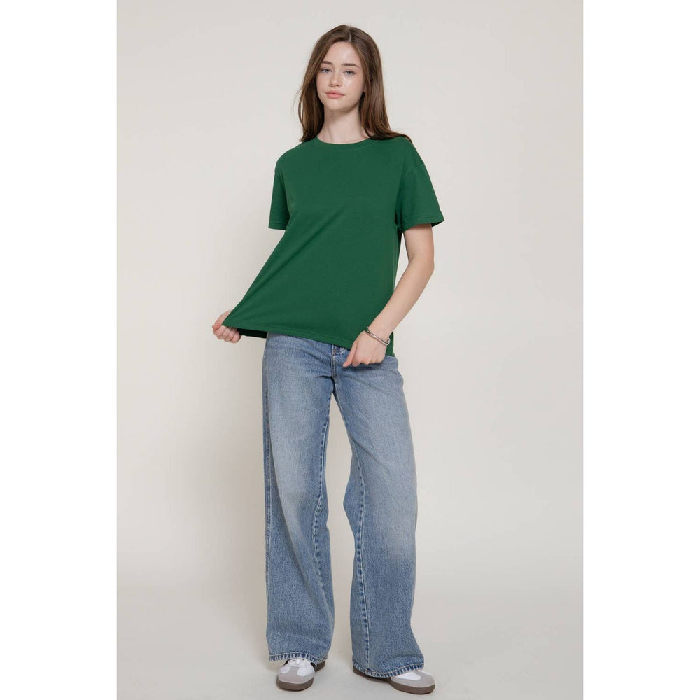 A woman wears a solid green short sleeve round neck tee with a relaxed fit made of soft breathable fabric
