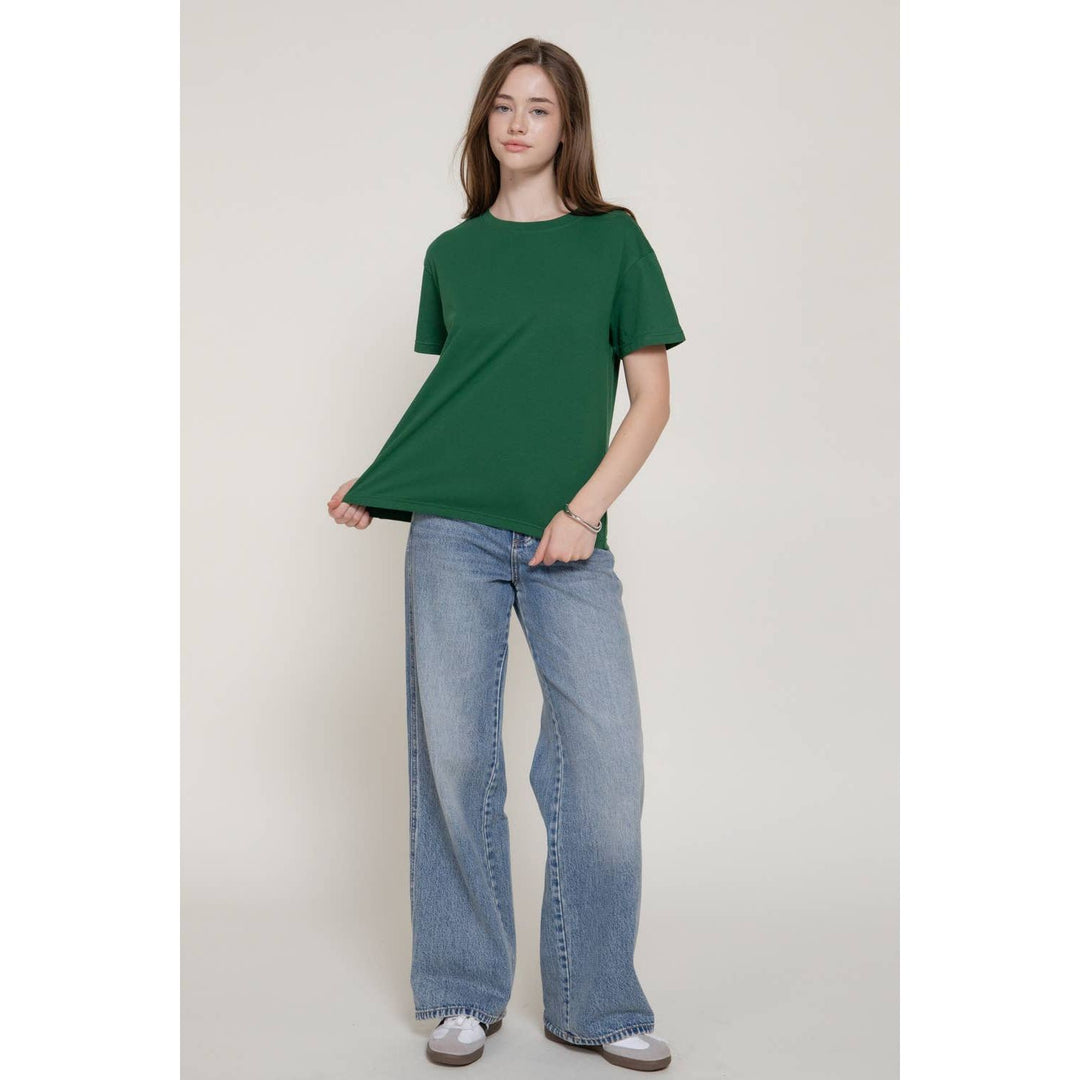 A woman wears a solid green short sleeve round neck tee with a relaxed fit made of soft breathable fabric