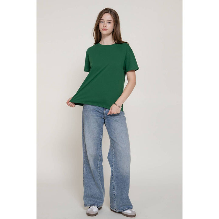 A woman wears a solid green short sleeve round neck tee with a relaxed fit made of soft breathable fabric