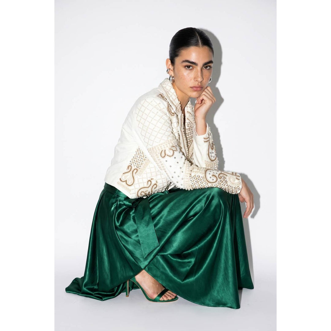 A woman wearing a white quilted jacket with gold embroidery and a glossy green satin maxi skirt