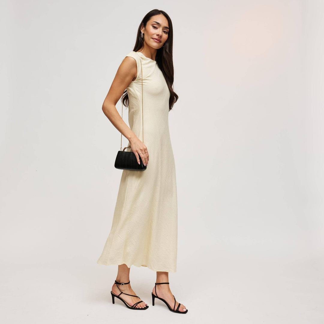A woman wearing a flowing cream sleeveless midi dress holds a black nichelle clutch with a sleek design