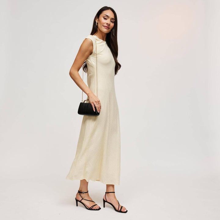 A woman wearing a flowing cream sleeveless midi dress holds a black nichelle clutch with a sleek design