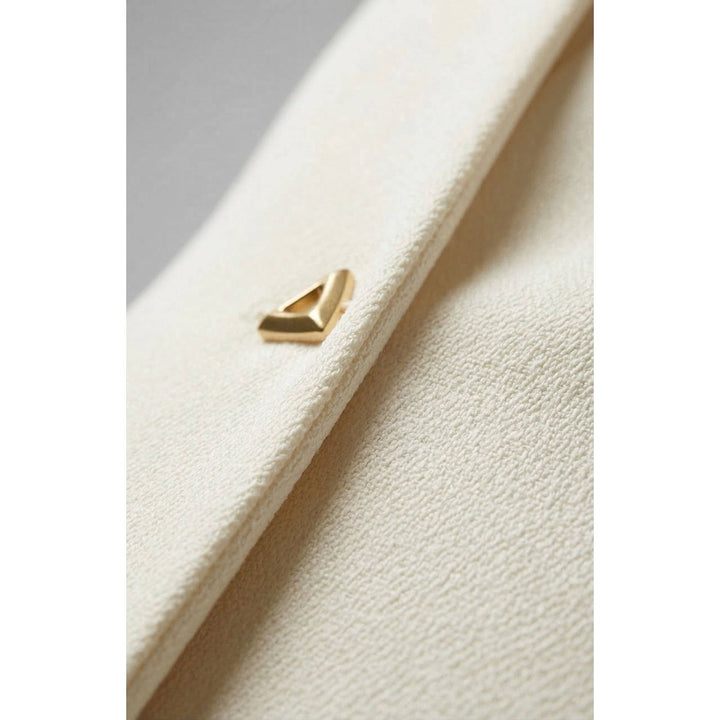 A textured wrap top with cream-colored fabric and a gold-tone triangular metal clasp detail