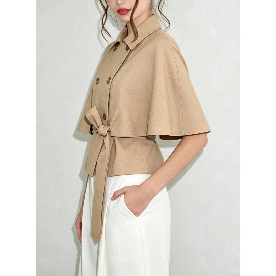 Beige double-breasted cape top with collar and matching belt tied at the waist in a cape-style coat design