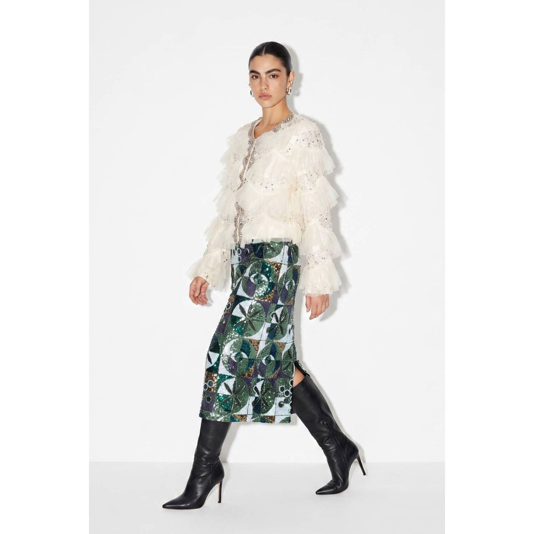 A woman wears a sequin embellished skirt with an intricate green black and silver geometric pattern and a white blouse