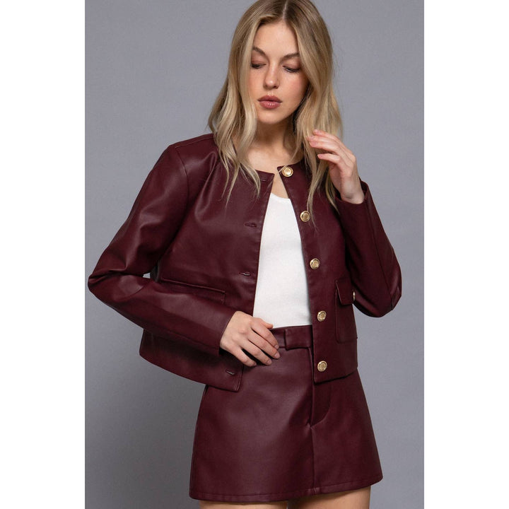 Burgundy cropped jacket in maroon faux leather with gold-tone buttons paired with matching mini skirt