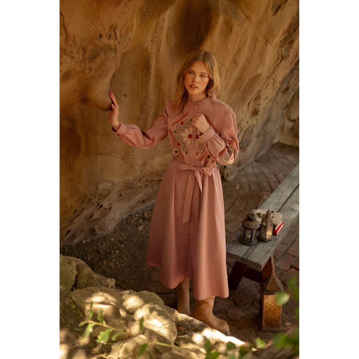 A soft pink embroidered shirtdress with long sleeves and a matching belt tied at the waist