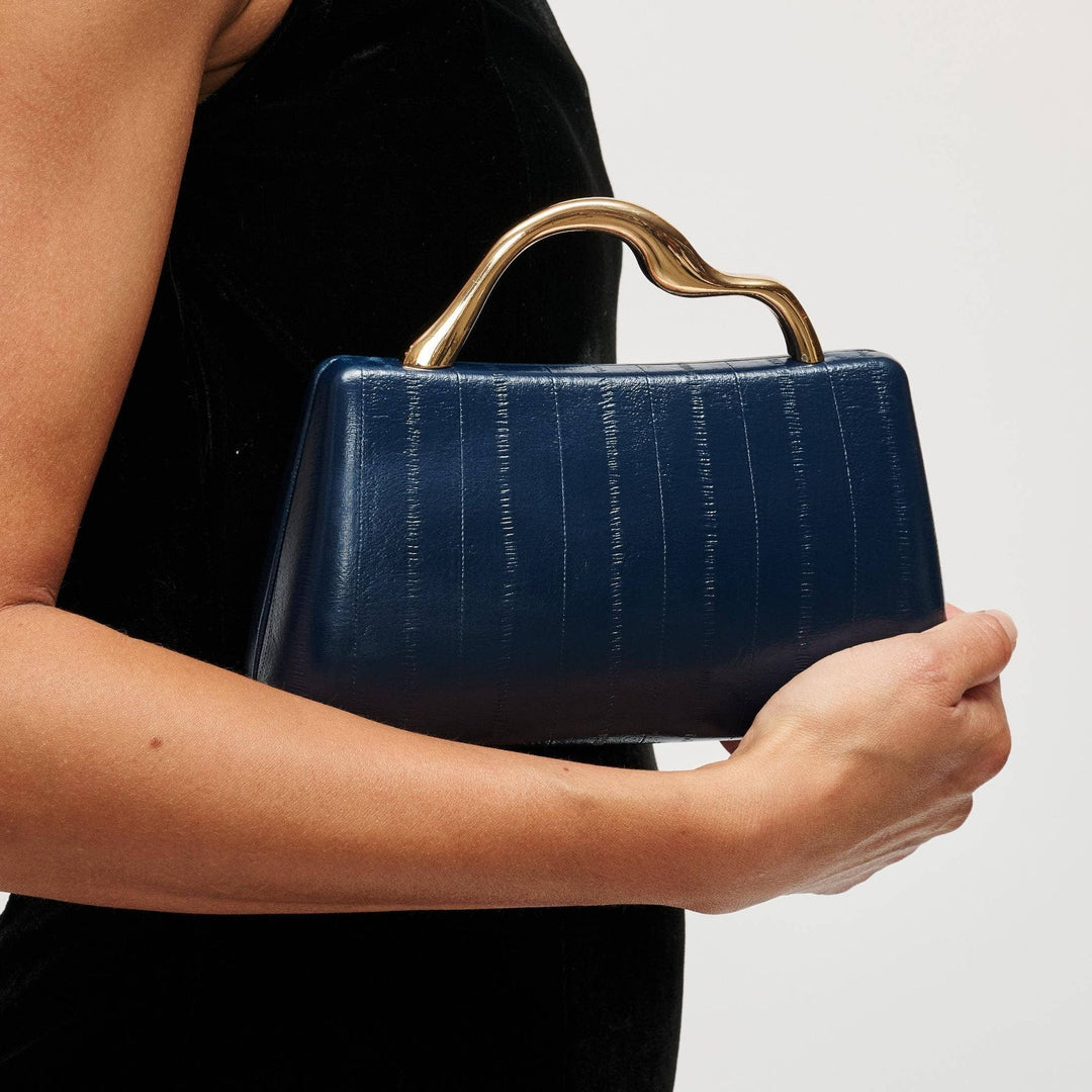 Deep blue nichelle clutch in crocodile embossed leather with a sculpted gold tone handle for elegant occasions