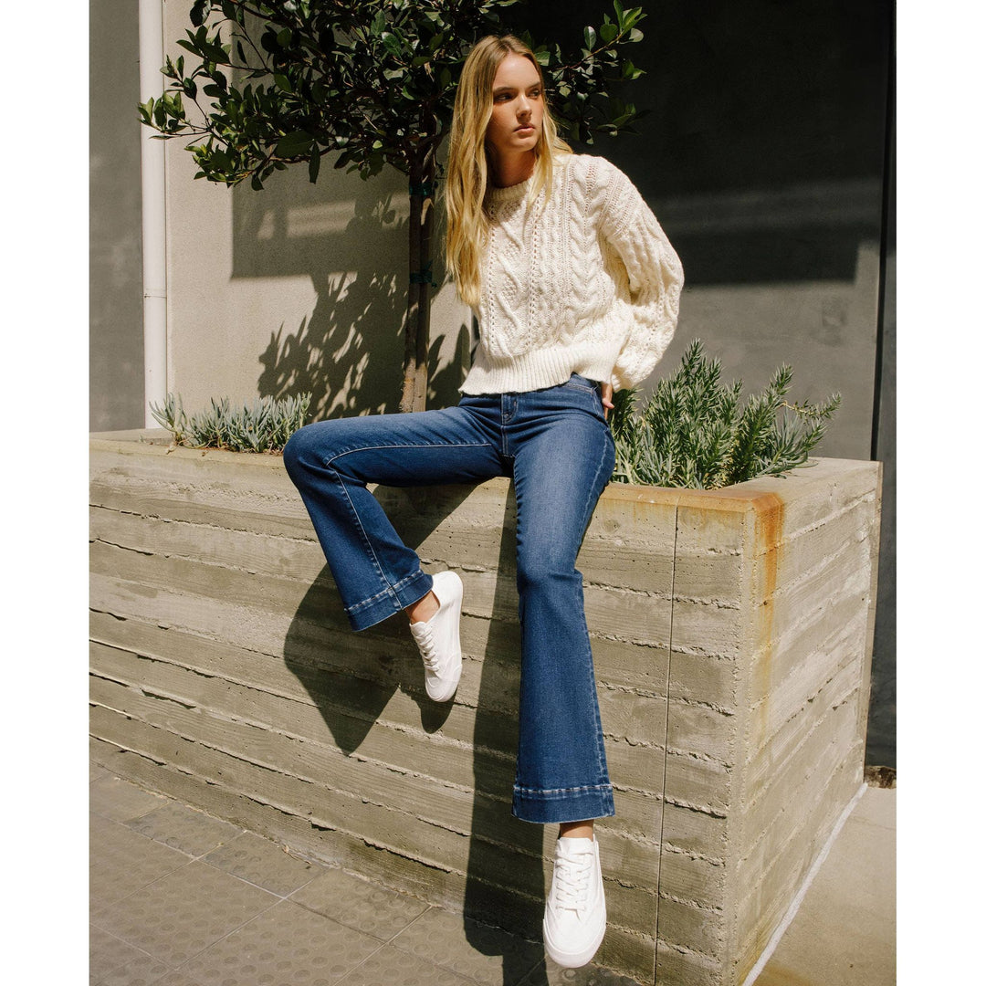 Cream-colored cable-knit sweater with textured intricate pattern and ribbed cuffs paired with high rise trouser denim
