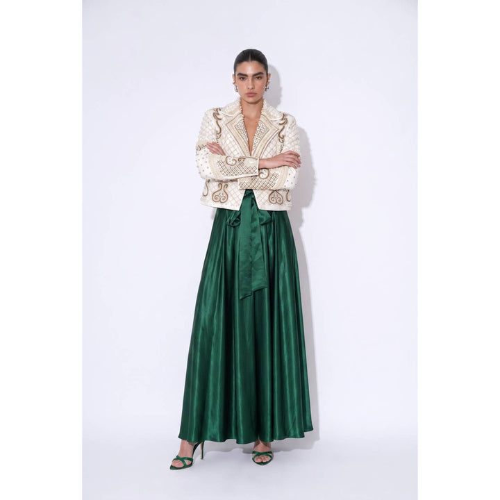 A woman wearing an ivory embroidered blazer with gold thread over a flowing emerald green glossy satin maxi skirt