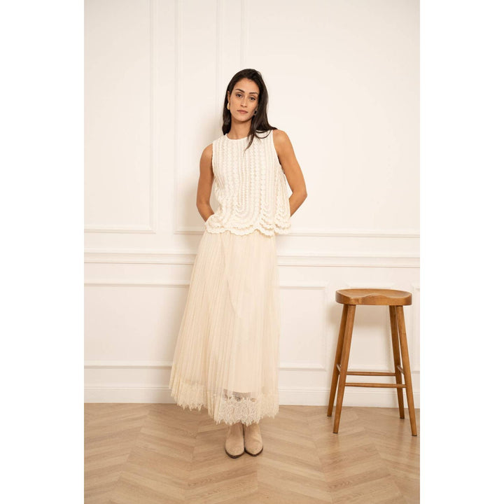 A woman wears an off-white embroidered tulle sleeveless top with ribbed detailing and ruffled hem paired with sheer skirt