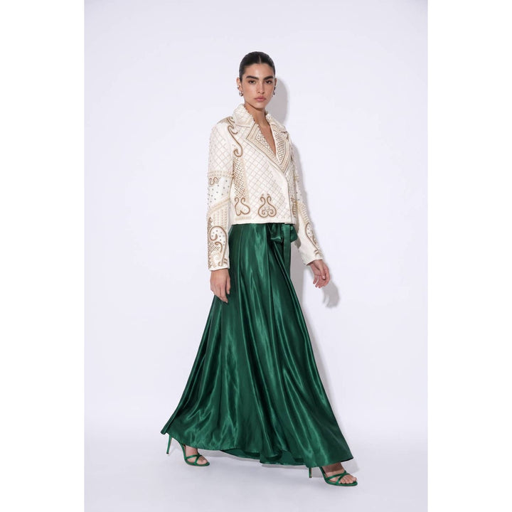 A woman wears an emerald green glossy satin maxi skirt with an ivory jacket featuring gold embroidery