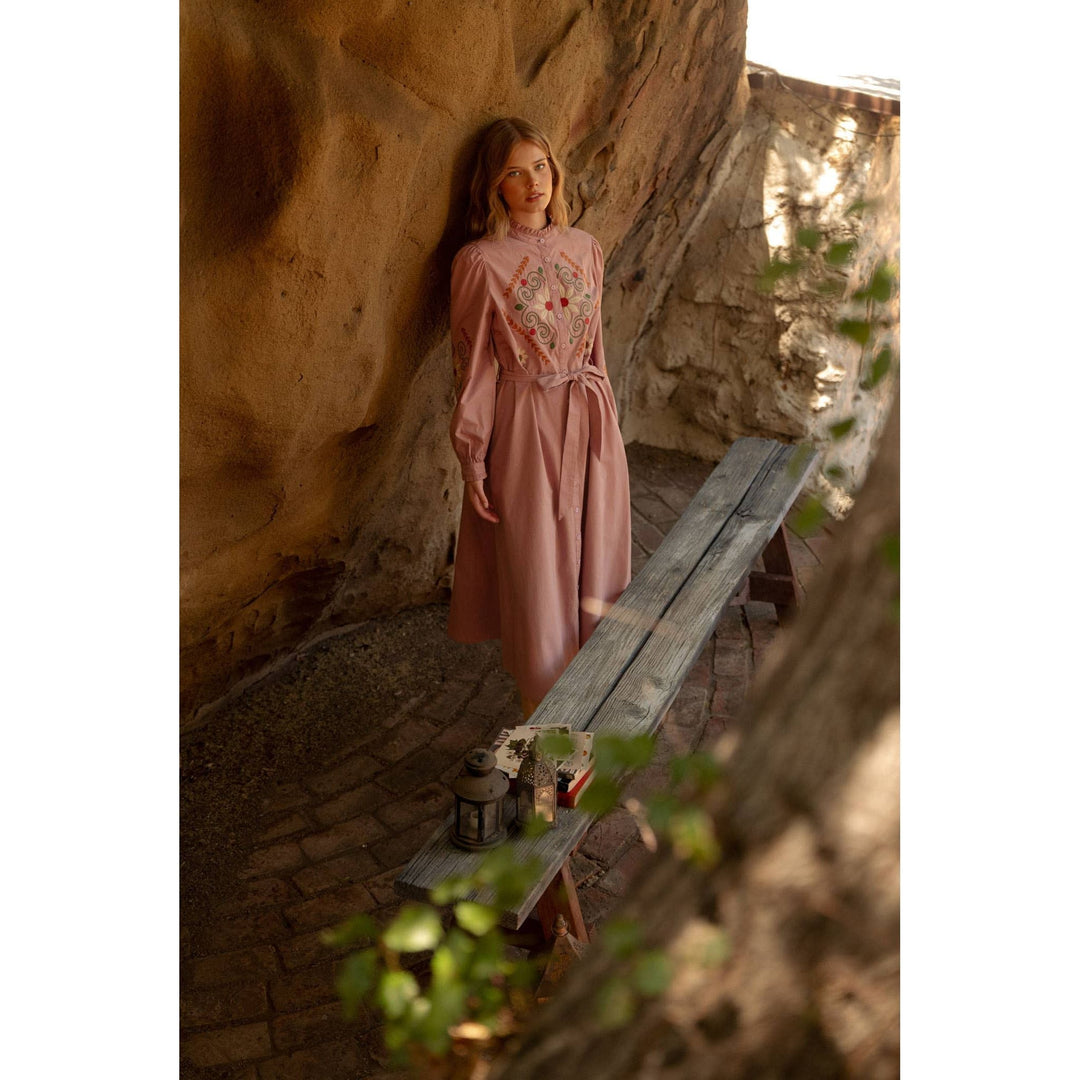A soft pink embroidered shirtdress with long sleeves and matching belt featuring intricate bodice detailing