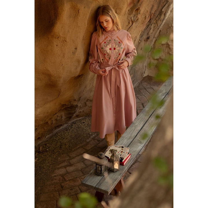 A soft pink embroidered shirtdress with long sleeves and intricate red and gold floral embroidery on the chest