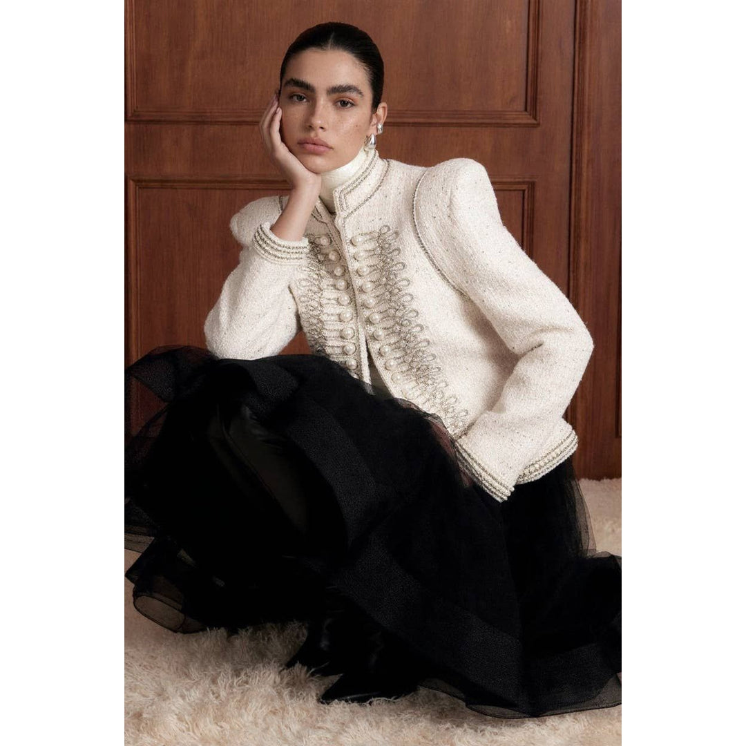 A cream-colored bouclé pearl embellished military jacket with silver-toned buttons and a high collar