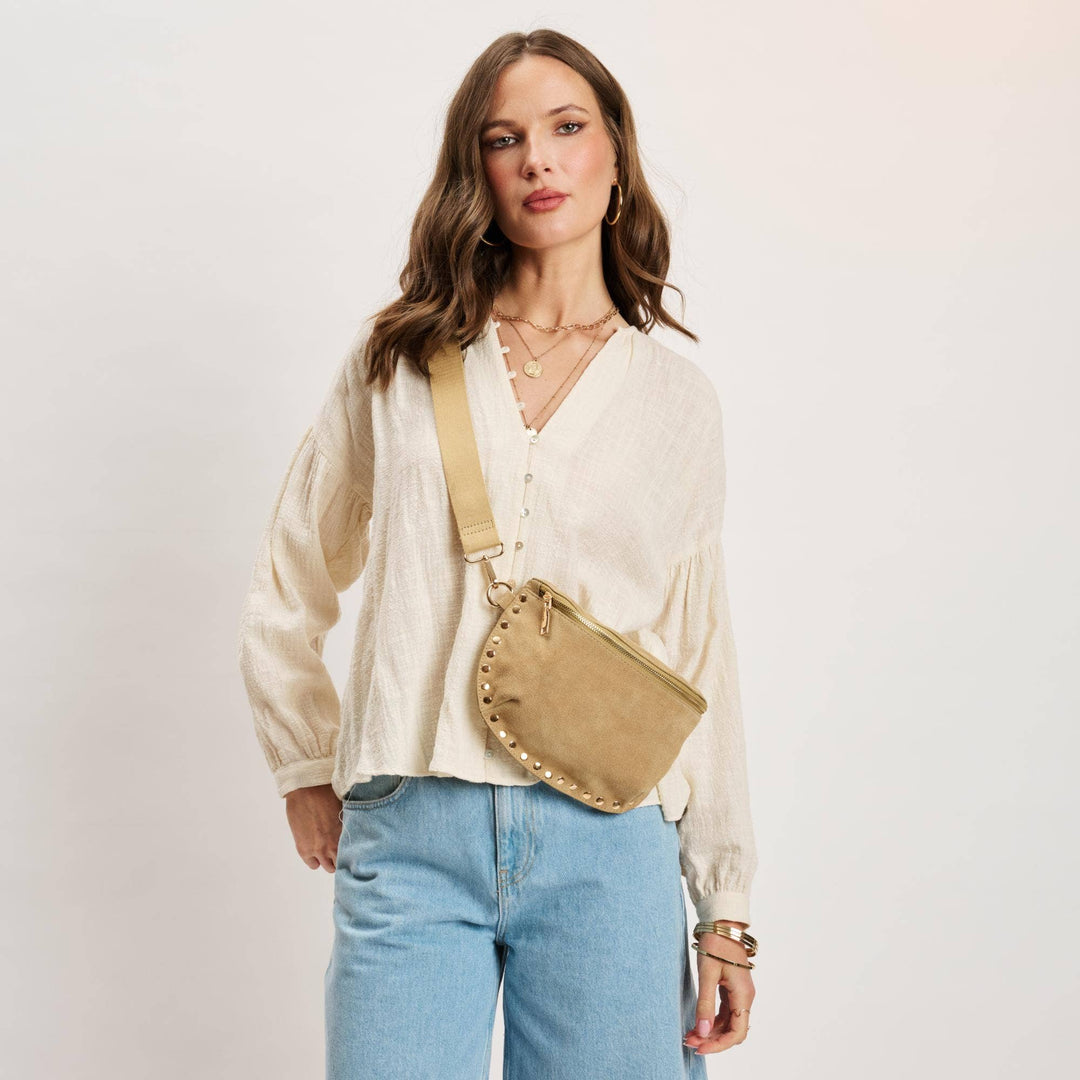 Beige suede gizelle-suede belt bag with gold-tone studs along curved edge and matching adjustable strap bone color