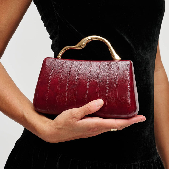 A nichelle clutch burgundy with a glossy crocodile-embossed surface and a sleek gold-tone handle