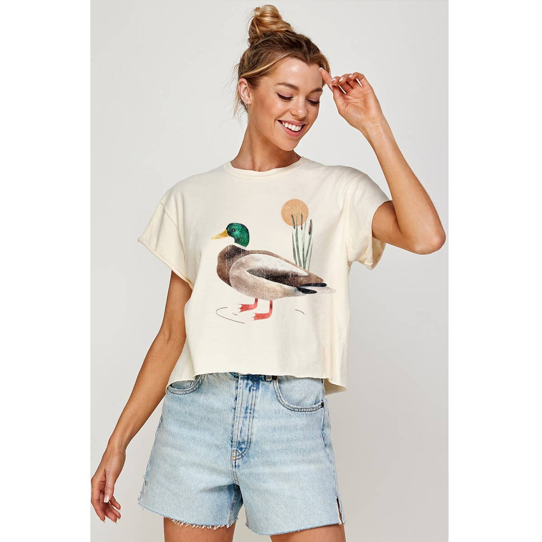 The Pearl Pagoda cream cotton crop tee featuring a vintage mallard duck illustration worn by a smiling woman.