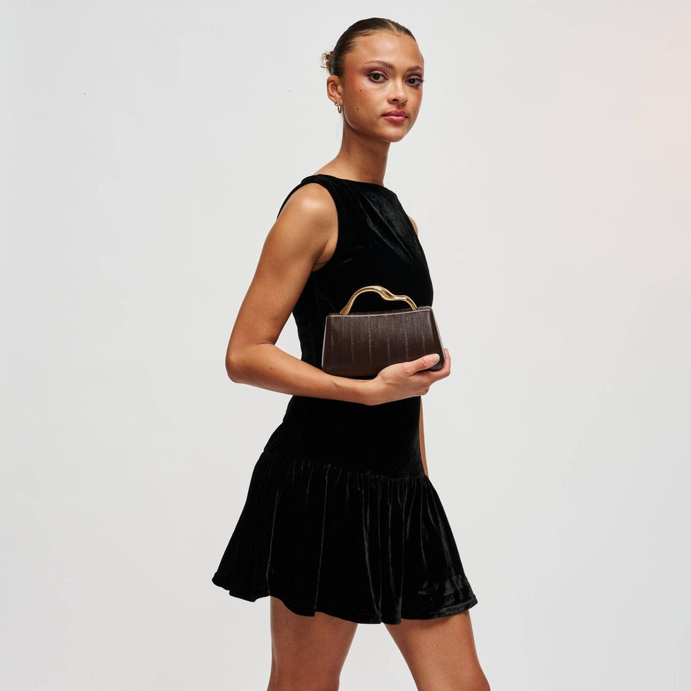 Model holding The Pearl Pagoda Nichelle Clutch in espresso brown with a sculptural gold handle and embossed texture.
