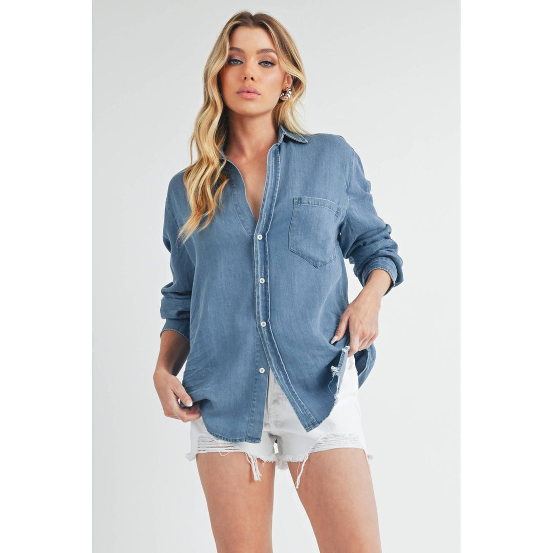 The Pearl Pagoda Ottavia denim top with a relaxed fit, raw shirttail hem, and chest pocket on a blonde model.