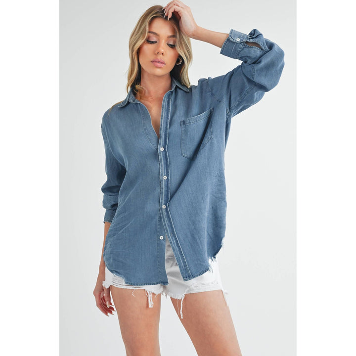 The Pearl Pagoda Ottavia denim top with a relaxed fit, chest pocket, and raw shirttail hem on a blonde model.
