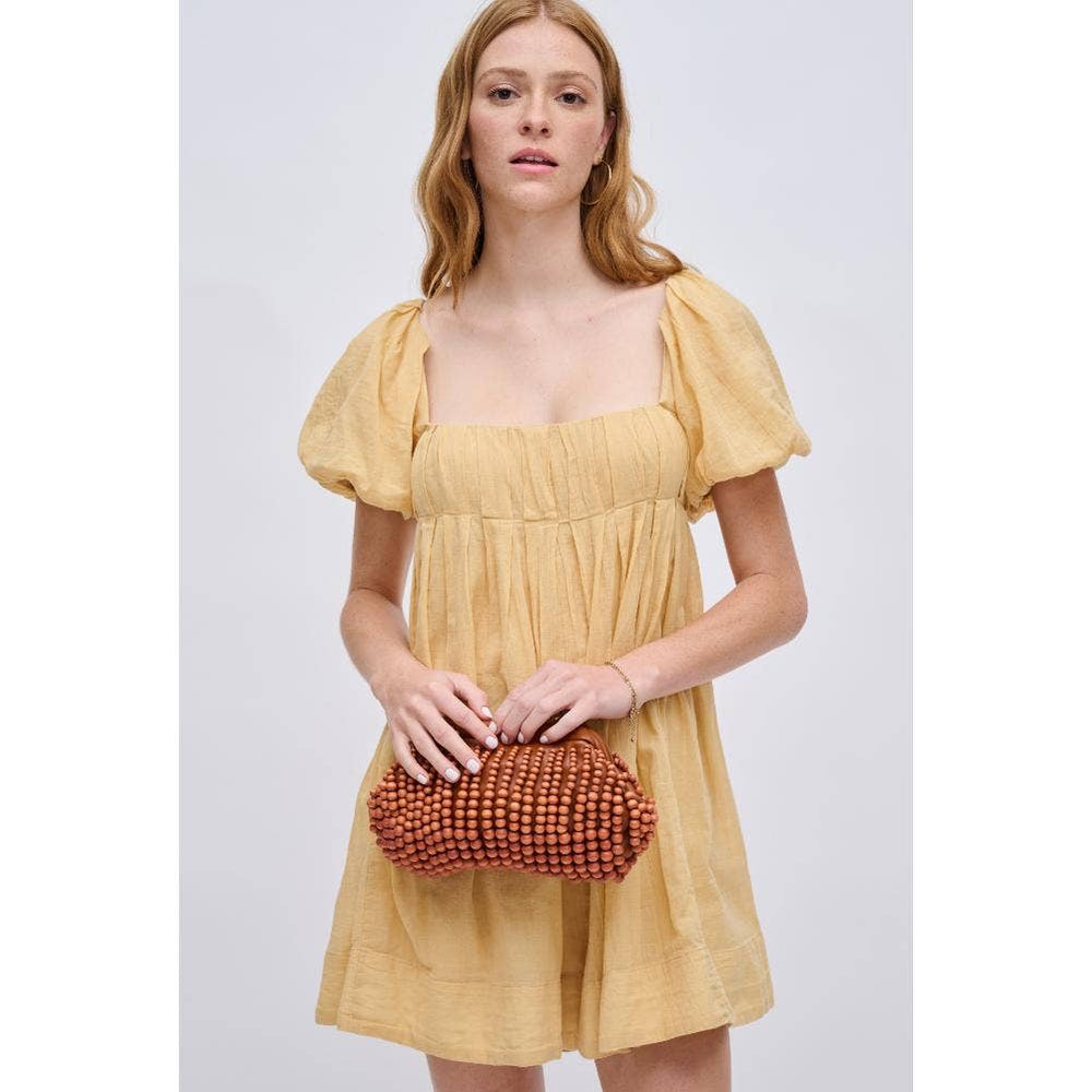 Model holding The Pearl Pagoda Lydia beaded teak wood clutch with a gold chain strap, wearing a yellow mini dress.