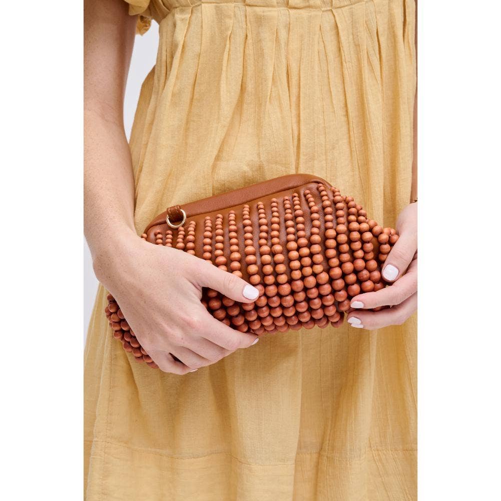 The Pearl Pagoda Lydia teak beaded clutch held by a woman in a yellow dress, featuring a gold detachable chain strap.