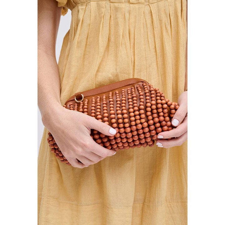 The Pearl Pagoda Lydia teak beaded clutch held by a woman in a yellow dress, featuring a gold detachable chain strap.