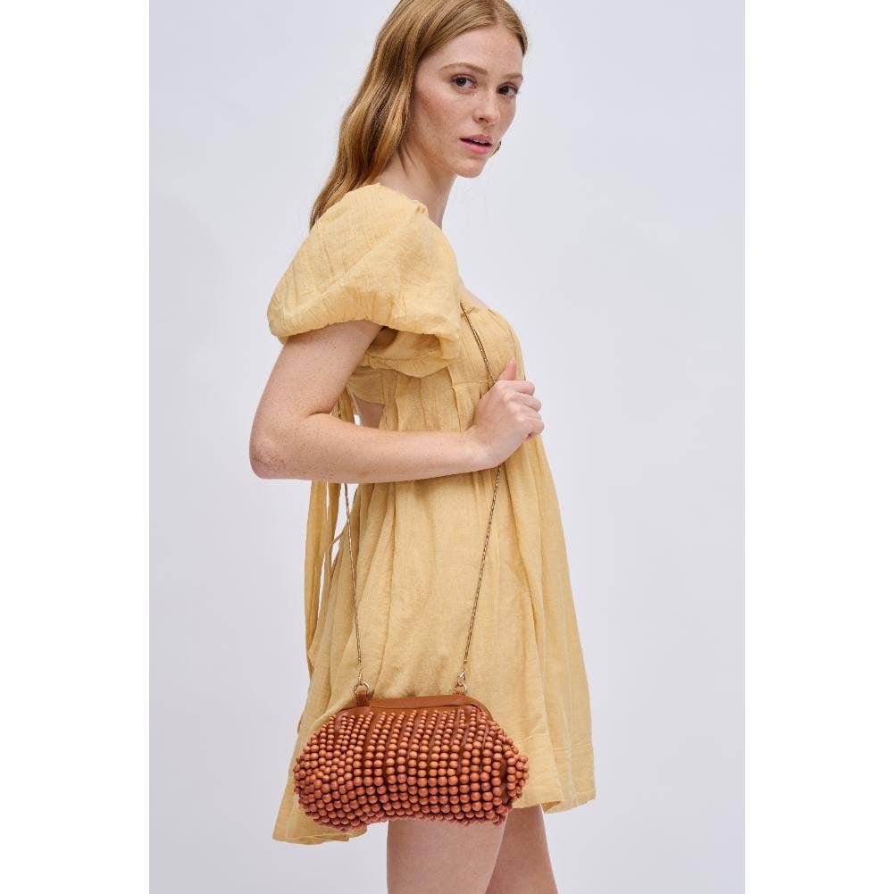 The Pearl Pagoda Lydia beaded teak wood clutch with a gold chain strap held by a woman in a yellow dress.